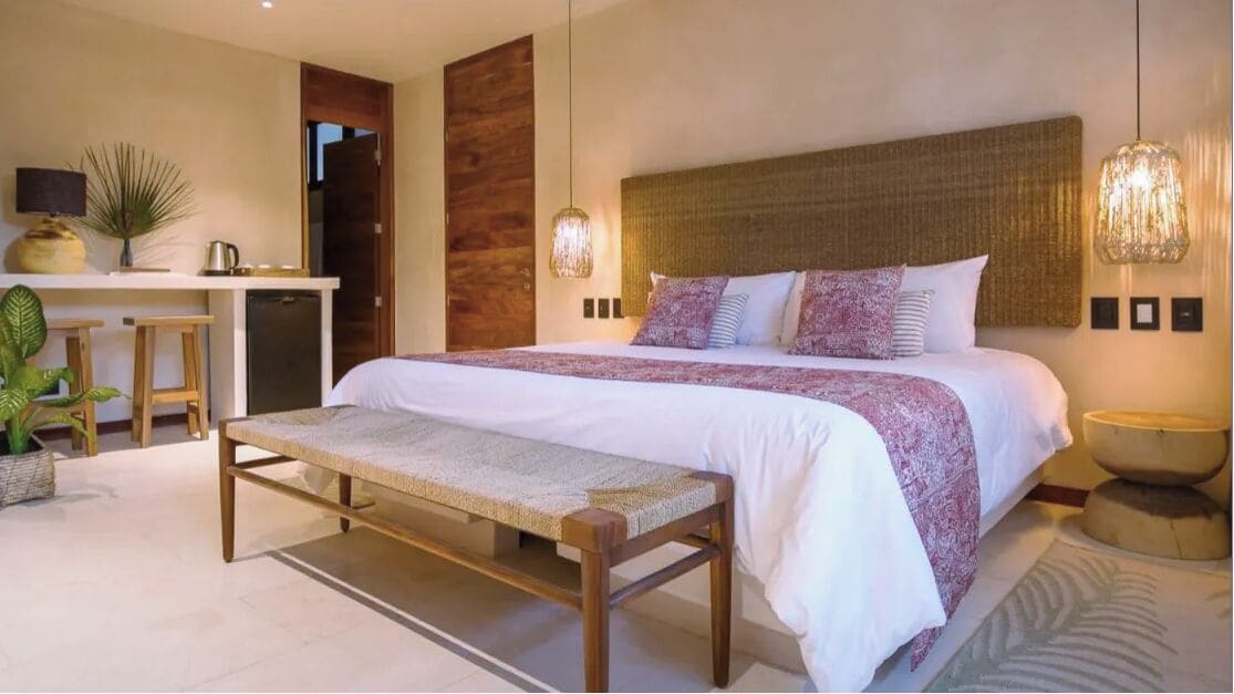 Un dormitorio moderno con una cama grande, un banco, un escritorio y una pequeña kitchenette.