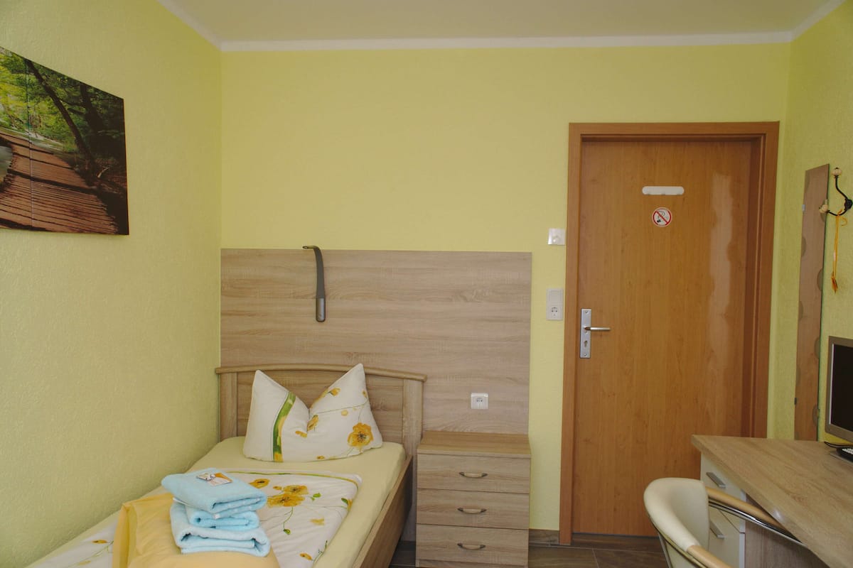 A bedroom with a bed, a wooden headboard, a nightstand, a desk, and a door.