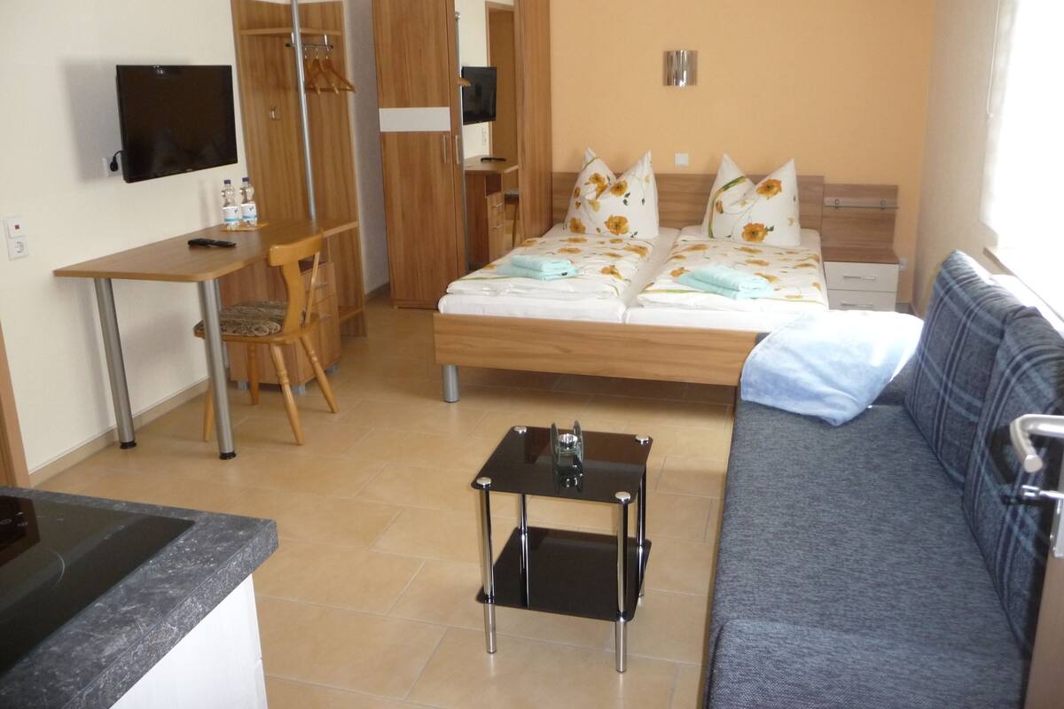 A compact hotel room with a bed, a sofa, a desk, and a TV.