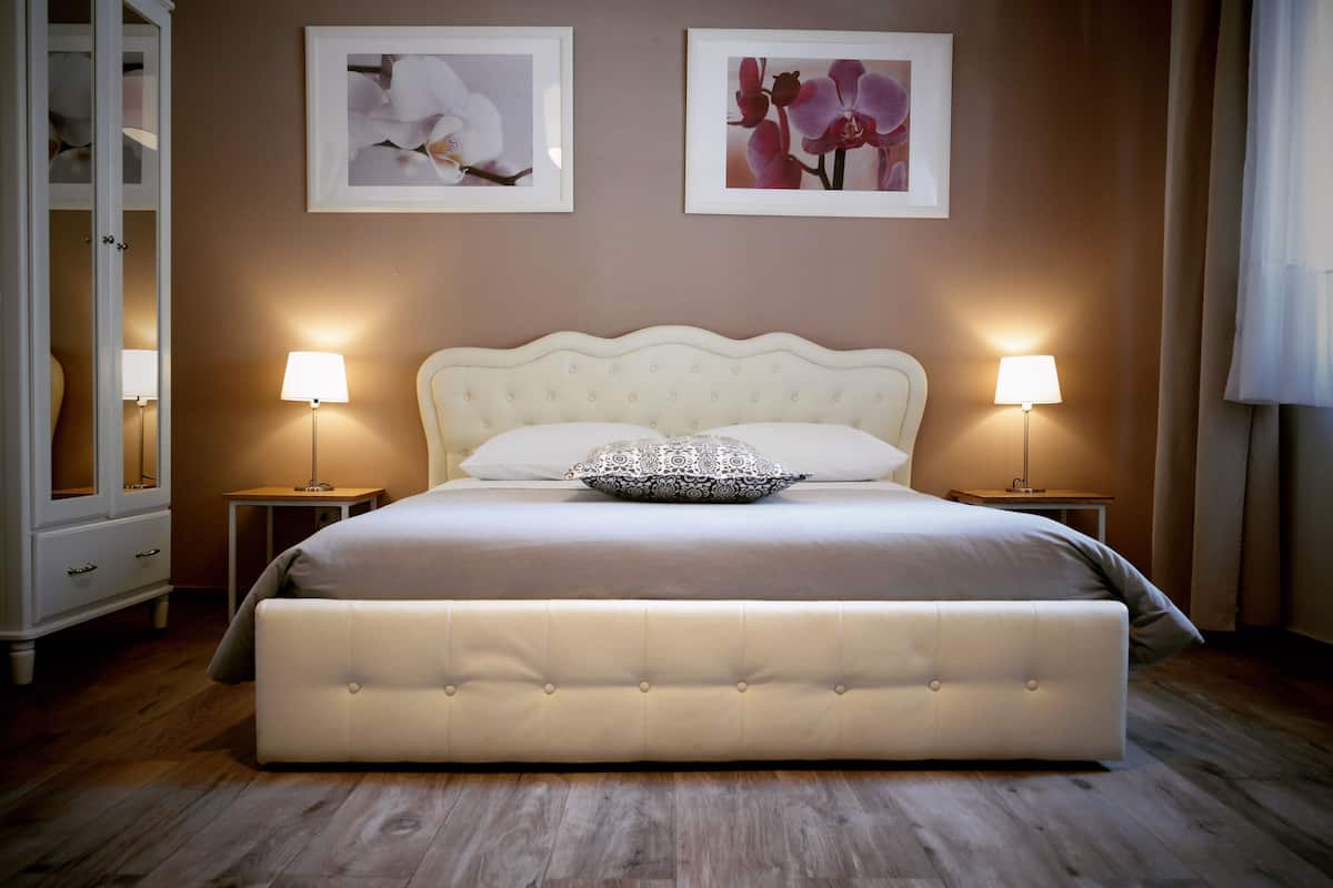 Ein Schlafzimmer mit einem großen Bett, zwei Nachttischen mit Lampen, einem Kleiderschrank und zwei gerahmten Bildern an der Wand.