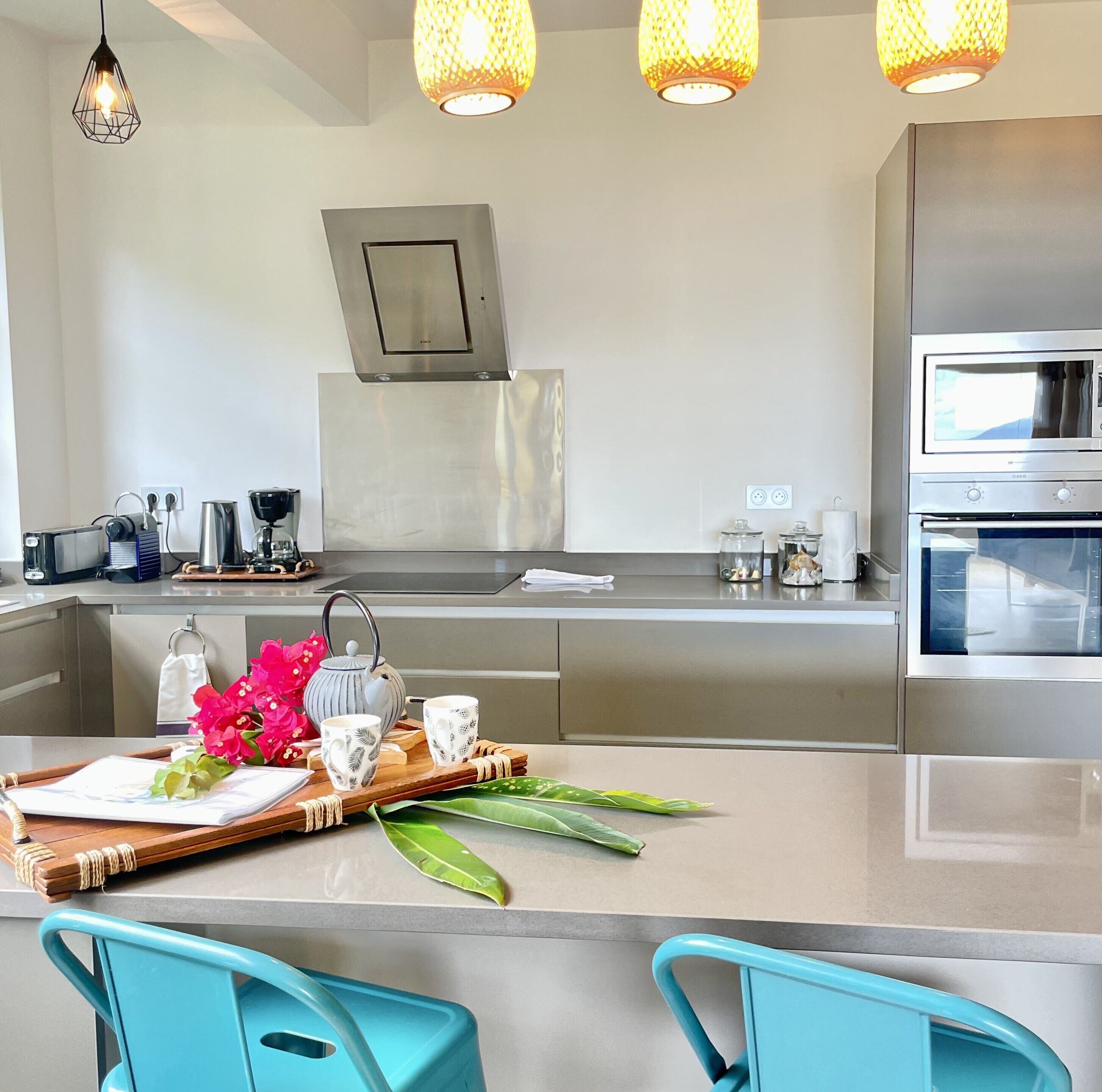 Een moderne keuken met roestvrijstalen apparatuur, een centraal eiland met een schaal bloemen, en teal-kleurige stoelen.