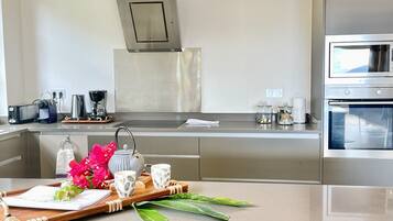 Een moderne keuken met roestvrijstalen apparatuur, een centraal eiland met een schaal bloemen, en teal-kleurige stoelen.