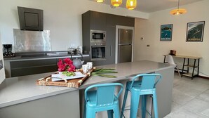 Une cuisine moderne dotée d’un îlot central, de tabourets de bar, d’appareils électroménagers en acier inoxydable et d’œuvres d’art décoratives murales.
