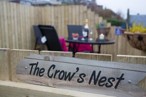 Une enseigne en bois portant l’inscription « The Crow’s Nest », placée dans un cadre extérieur rustique.