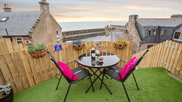 A patio with a round table and chairs, a wooden fence, and a view of the sea. - Amazing sea & harbour views of the Moray Firth North Aberdeenshire Scotland. (Macduff)