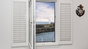 A window with shutters open, revealing a view of a lighthouse and a stone pier extending into the water. - Amazing sea & harbour views of the Moray Firth North Aberdeenshire Scotland. (Macduff)