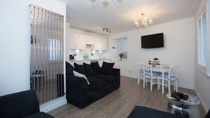 A modern living room with a black sofa, a dining area with a white table and chairs, and a kitchen in the background. - Amazing sea & harbour views of the Moray Firth North Aberdeenshire Scotland. (Macduff)