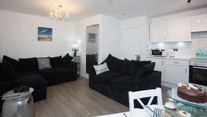 A modern living room with black sofas, a dining table with a cake, and a kitchen with white cabinets. - Amazing sea & harbour views of the Moray Firth North Aberdeenshire Scotland. (Macduff)