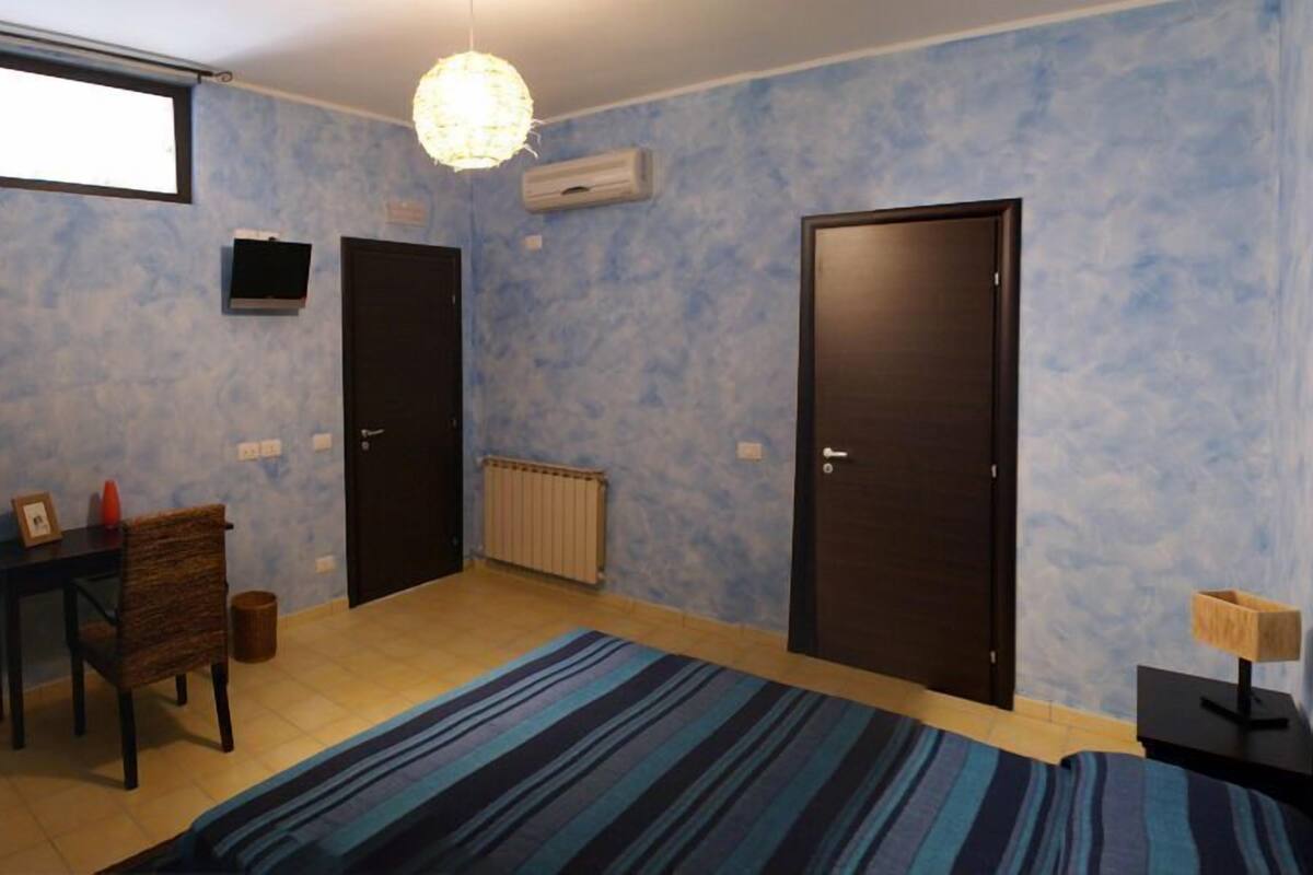 Un dormitorio con cama, escritorio, silla, radiador y dos puertas.