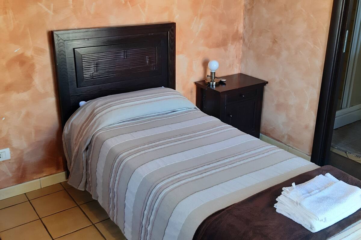 Un dormitorio con cama, mesita de noche, lámpara y baño visible a través de una puerta abierta.