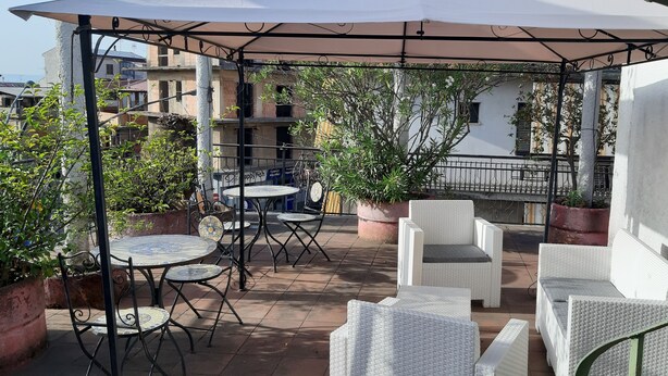 An outdoor patio with round tables and white wicker chairs, surrounded by potted plants and a pergola. - Le Antiche Colonne (Cinquefrondi)