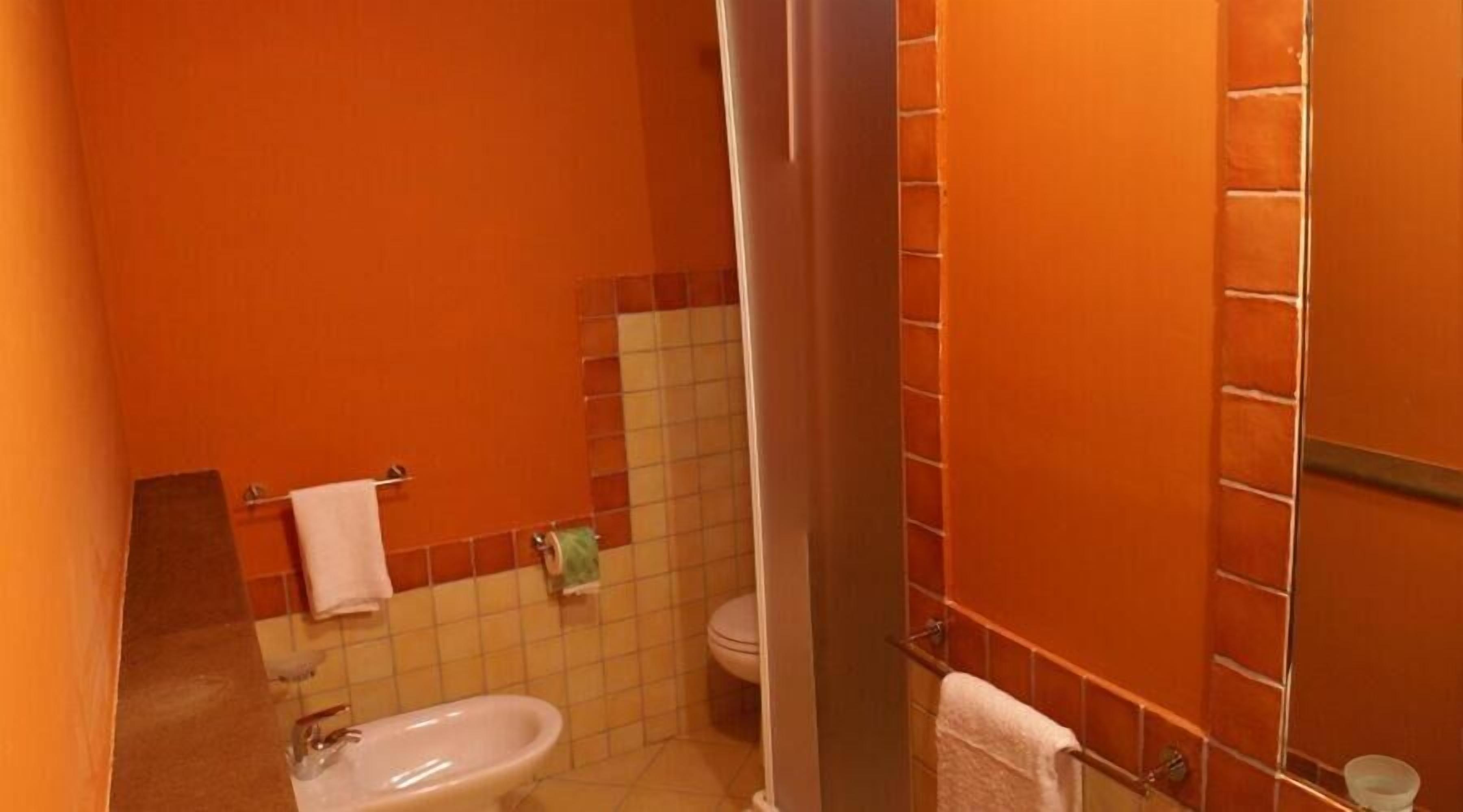A bathroom with orange walls, a white sink, and a toilet.