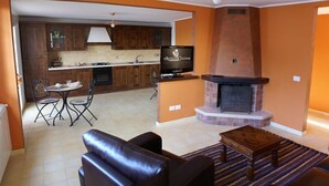 A modern living room with a fireplace, a dining area with a table and chairs, and a kitchen with wooden cabinets and a television. - Le Antiche Colonne (Cinquefrondi)