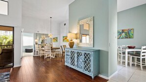 Un vaste espace dédié à la salle à manger, avec une table et des chaises en bois, un buffet bleu et un grand miroir accroché au mur.