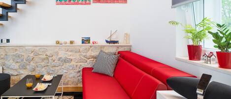 A modern living room with a red sofa, a black coffee table, and a stone wall.