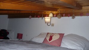 Ett sovrum med en säng, kuddar, en väggmonterad lampa och ett träpanelat tak.