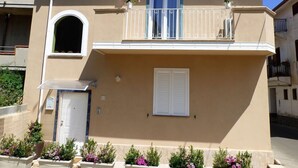A two-story building with a balcony, a door, and flower planters. - Aramoni B&B (Zambrone)