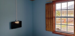 A room with a television mounted on the wall, a window with wooden shutters, and a view of a fenced outdoor area. - Pousada Ferreira's (Santo André)