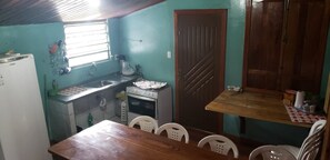 A compact kitchen with a refrigerator, stove, sink, and a dining area with chairs. - Pousada Ferreira's (Santo André)