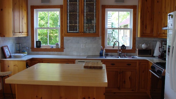 A kitchen with wooden cabinets, a central island, a double sink, and a stove. - Lake Chautauqua Victorian (Dewittville)