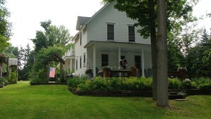 A two-story house with a porch, surrounded by a well-maintained lawn and trees. - Lake Chautauqua Victorian (Dewittville)