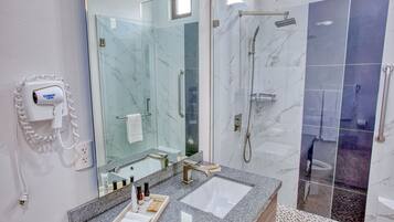 A modern bathroom with a glass-enclosed shower, a marble-tiled wall, a granite countertop, and a hairdryer mounted on the wall.