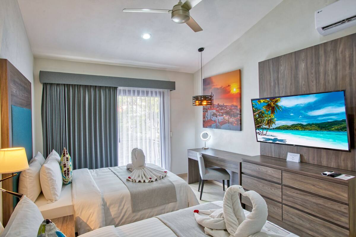 A hotel room with a bed, a desk, a chair, a TV, and a window with curtains.