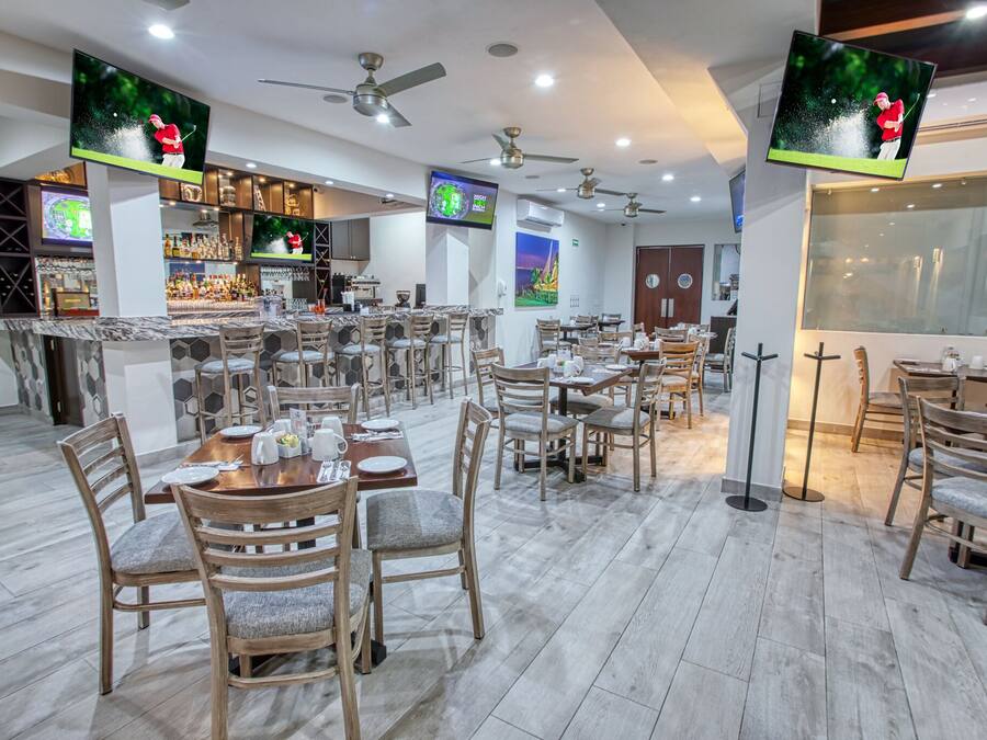 A restaurant with multiple tables and chairs, ceiling fans, and televisions displaying golf scenes.