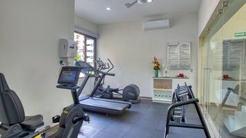 A gym with treadmills, stationary bikes, and a weight bench. There is a wall-mounted air conditioner and a ceiling fan.