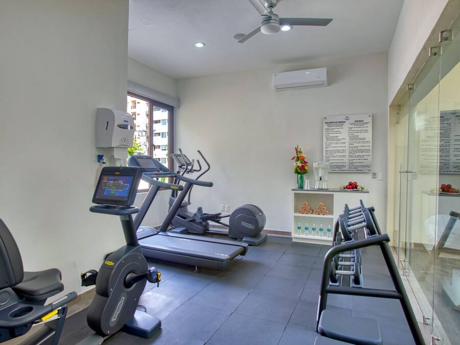 A gym with treadmills, stationary bikes, and a weight bench. There is a wall-mounted air conditioner and a ceiling fan.