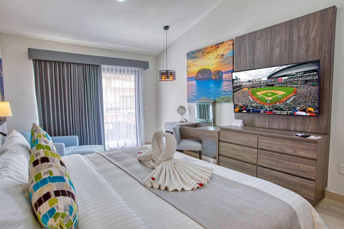 A hotel room with a bed, a desk, a television, and a view of a baseball stadium.