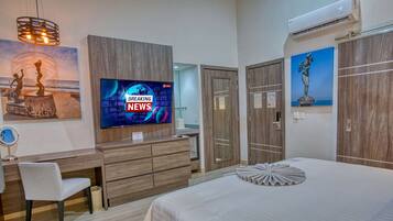 A modern hotel room with a large bed, a wooden desk, a television displaying news, and artwork on the walls.