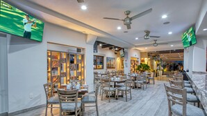 A modern restaurant with multiple dining areas, ceiling fans, and flat-screen TVs displaying sports. - Casa Nicole Boutique Hotel (Puerto Vallarta)