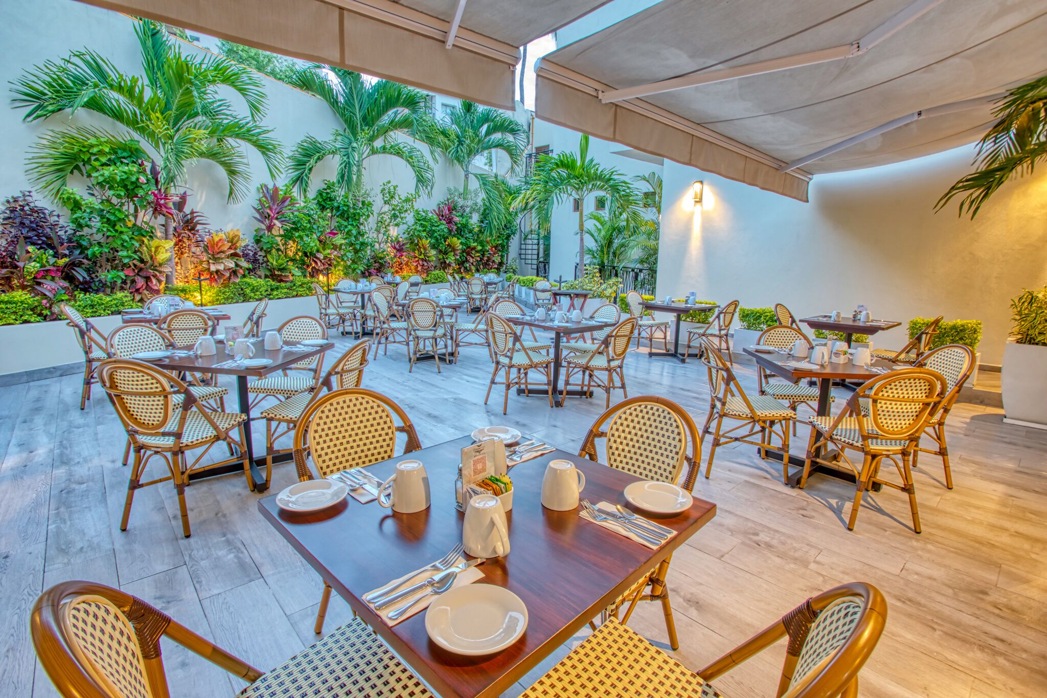 A restaurant with outdoor seating, wicker chairs, and tables set with plates and cutlery.