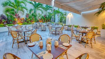 A restaurant with outdoor seating, wicker chairs, and tables set with plates and cutlery.