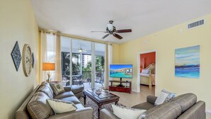 A living room with a sofa set, a coffee table, a TV, and a balcony with a view of the sea. - Regatta - William Raveis Rentals (Naples)