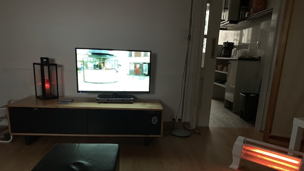 Ein Wohnzimmer mit Flachbildfernseher auf Holzständer, Stehlampe, Heizung und Sofa.