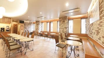 A hotel dining area with multiple tables and chairs, stone accent walls, and large windows.
