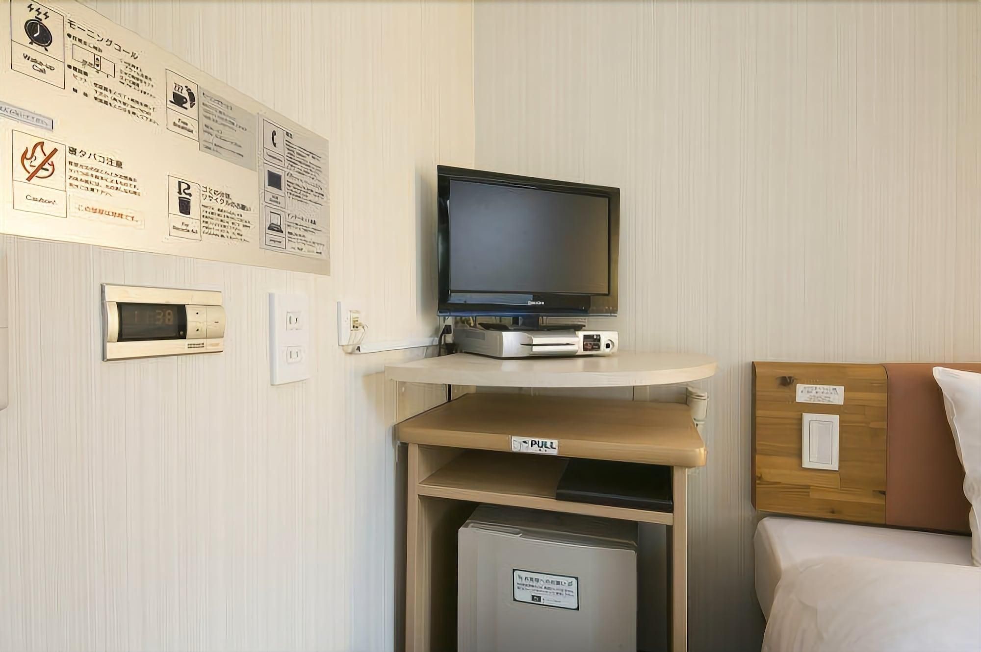 Una camera d'albergo con televisore su un mobile, un piccolo frigorifero e un letto con testiera in legno.