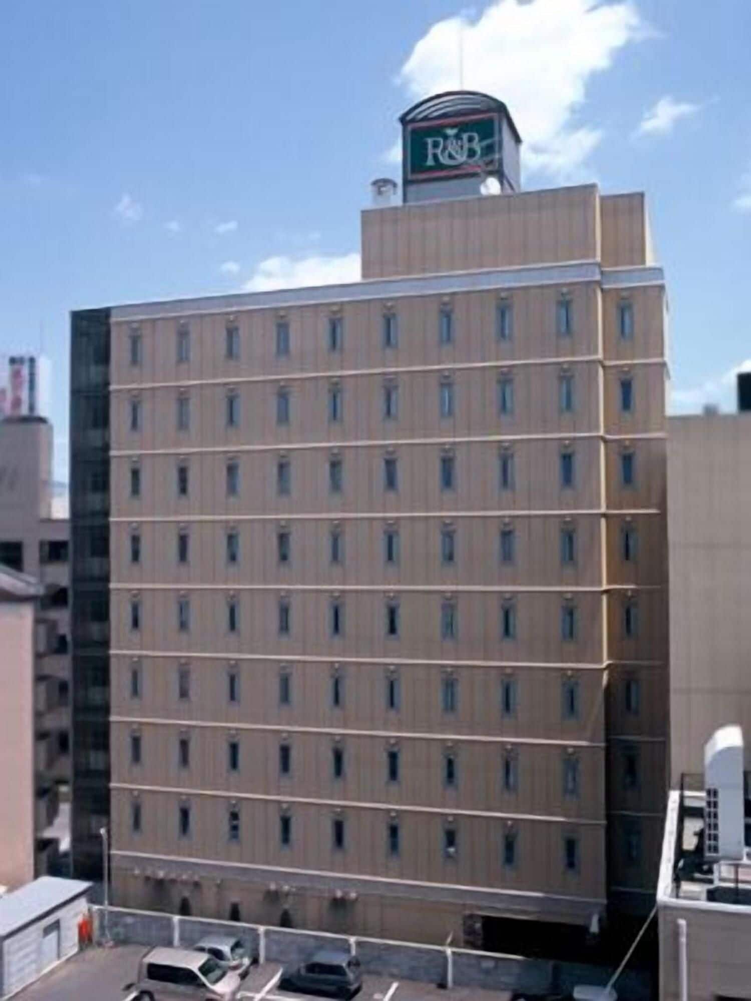 Un hotel de varios pisos con un llamativo letrero de R&B en la parte superior, que presenta una fachada uniforme con ventanas distribuidas regularmente.