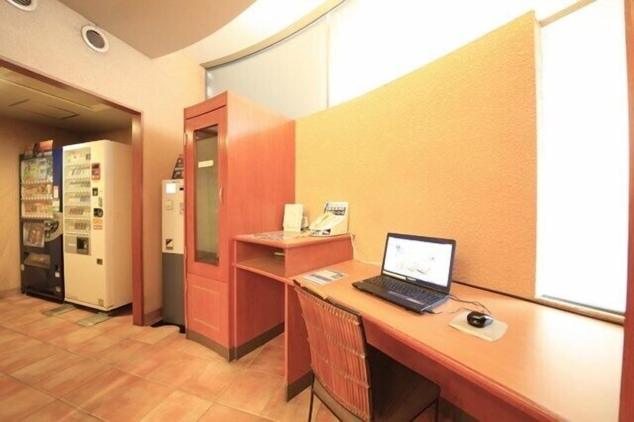 A hotel room with a desk, a computer, a telephone, and vending machines.