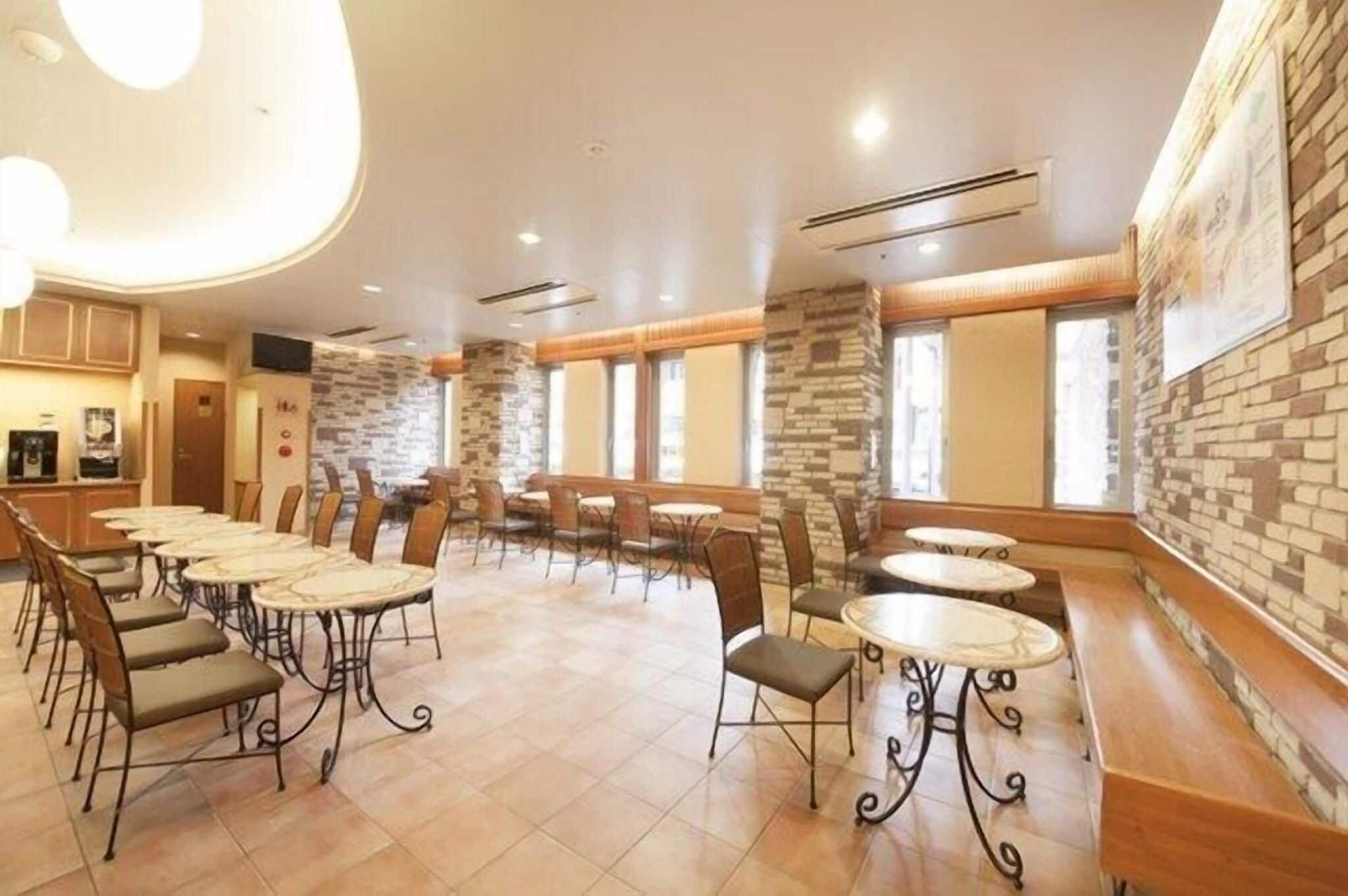 Un amplio comedor interior con varias mesas y sillas, paredes de acento de piedra y ventanas grandes.