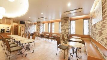 Un amplio comedor interior con varias mesas y sillas, paredes de acento de piedra y ventanas grandes.