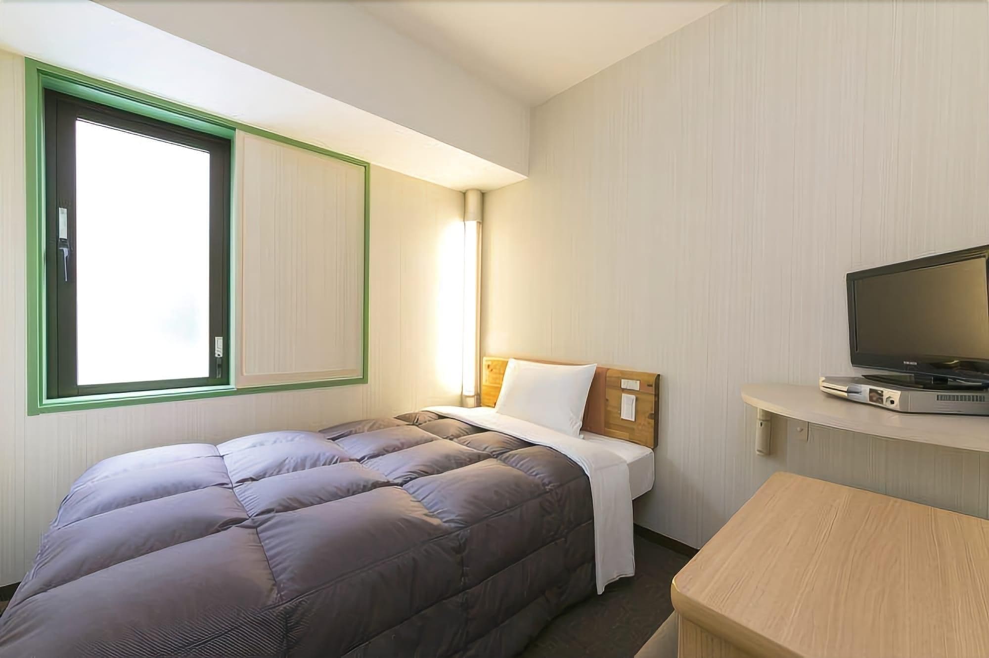 A hotel room with a bed, a television, and a window.