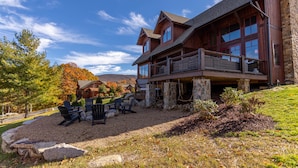A large wooden lodge with a stone foundation, outdoor seating area, and a view of the surrounding landscape. - Red, White and Views at Eagles Nest- club amenities, hot tub, long range views, pet friendly (Banner Elk)