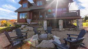 A large wooden house with a balcony, outdoor seating area with Adirondack chairs, and a fire pit. - Red, White and Views at Eagles Nest- club amenities, hot tub, long range views, pet friendly (Banner Elk)