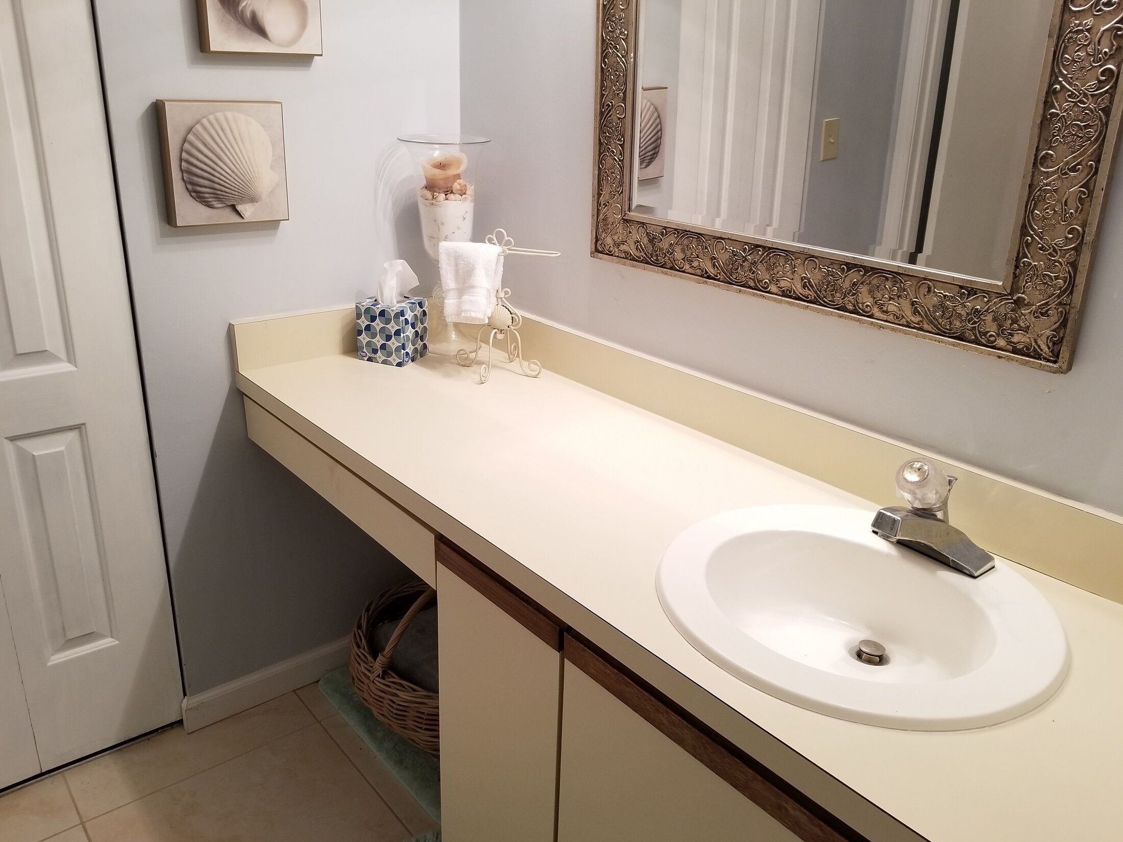 A bathroom with a white sink, a mirror with an ornate frame, and decorative shells on the wall.