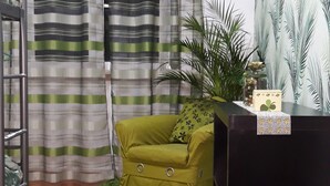 A room with a green sofa, a black desk, a striped curtain, a wooden floor, and a wall with a palm tree pattern. - Ameli Rooms (Lisbon)