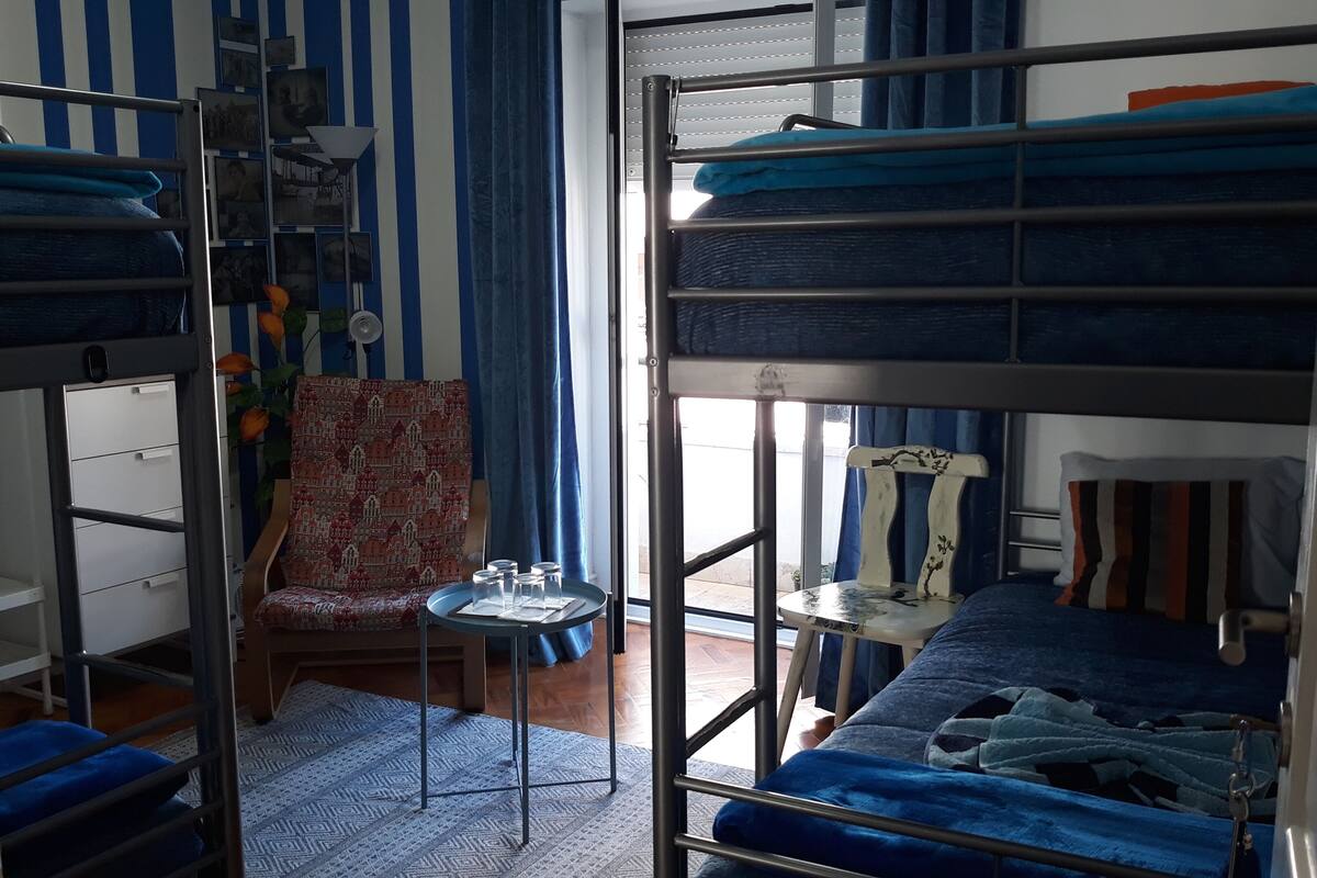 A dormitory room with bunk beds, a chair, a small table with glasses, and a window with curtains.