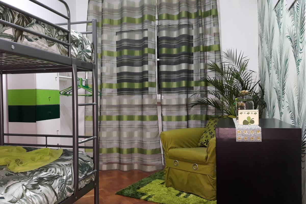 A bunk bed room with a green and white striped curtain, a small desk with a plant, and a green chair.